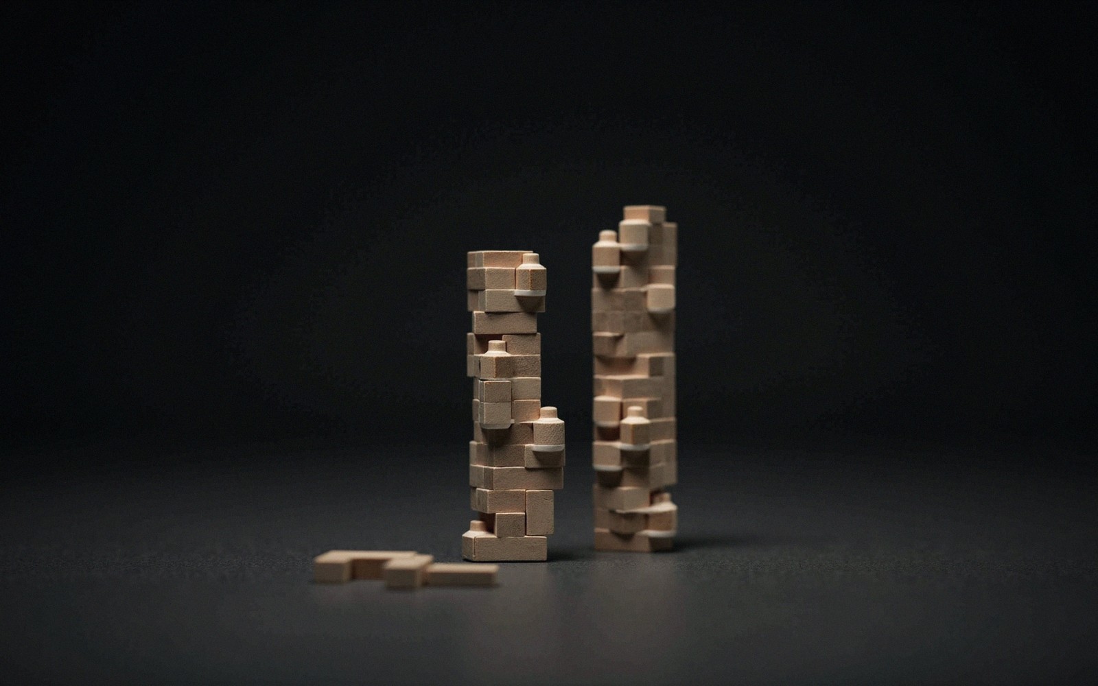 Two irregular wooden block towers stand beside scattered pieces on a dark surface